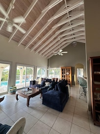 Living room area with a dining table, sectional couch, wicker chairs, tv, games, books, island magazines