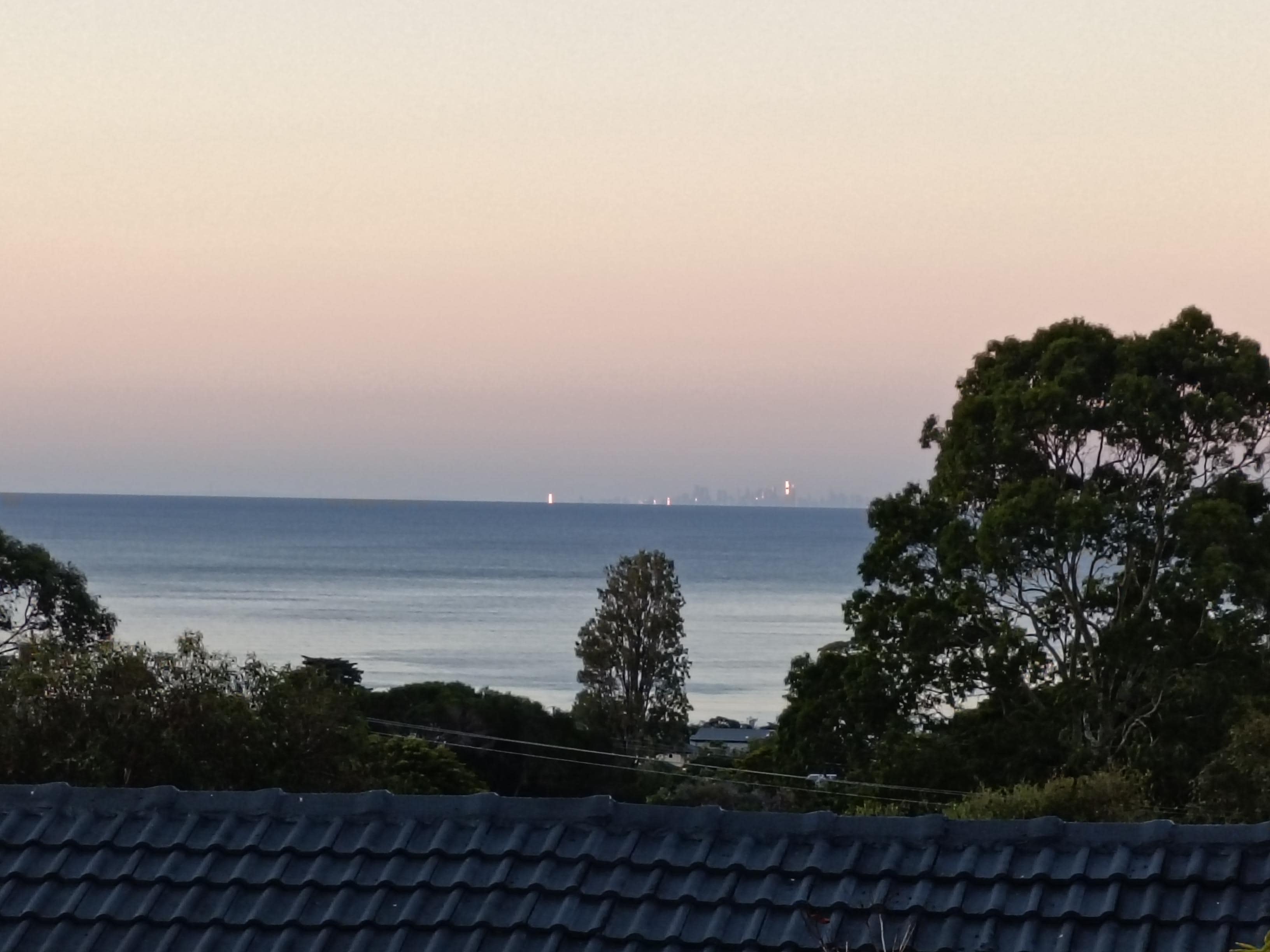 Setting sun glinting off the Melbourne skyline in the distance, across Port Philip Bay from the deck of the Dromana holiday house