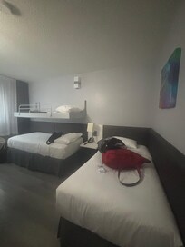 A compact but functional room featuring two single beds and a bunk bed above. The design is simple, with dark furniture and white linens.