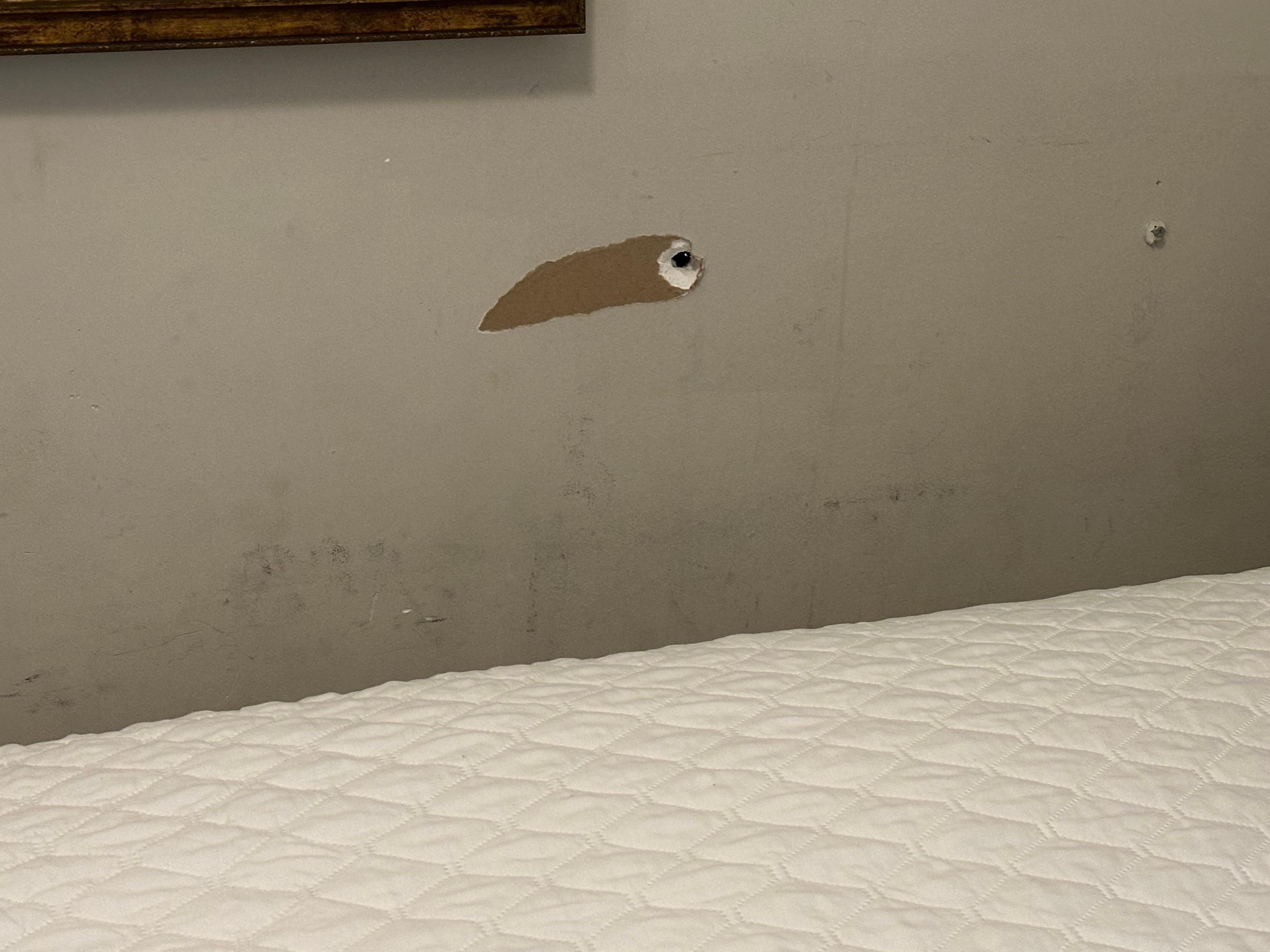 Holes and dirty walls next to the bed