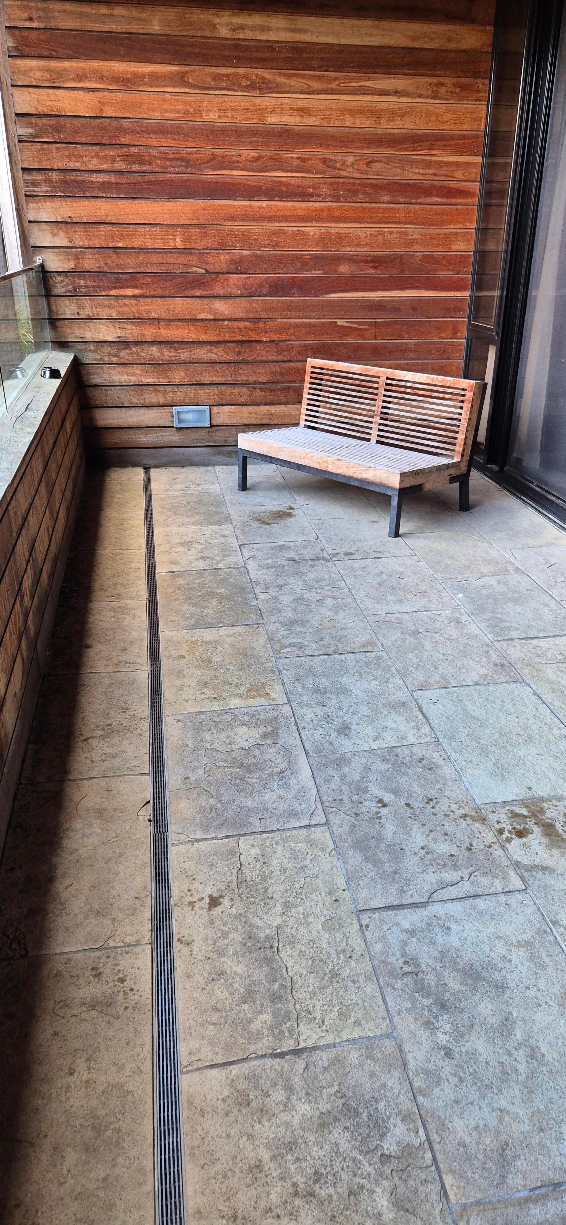 Outdoor balcony space but no outdoor furniture besides 1 old wooden  bench with no cushions. 