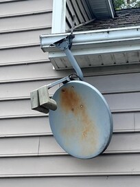 Satellite dish hanging by a wire from the roof.