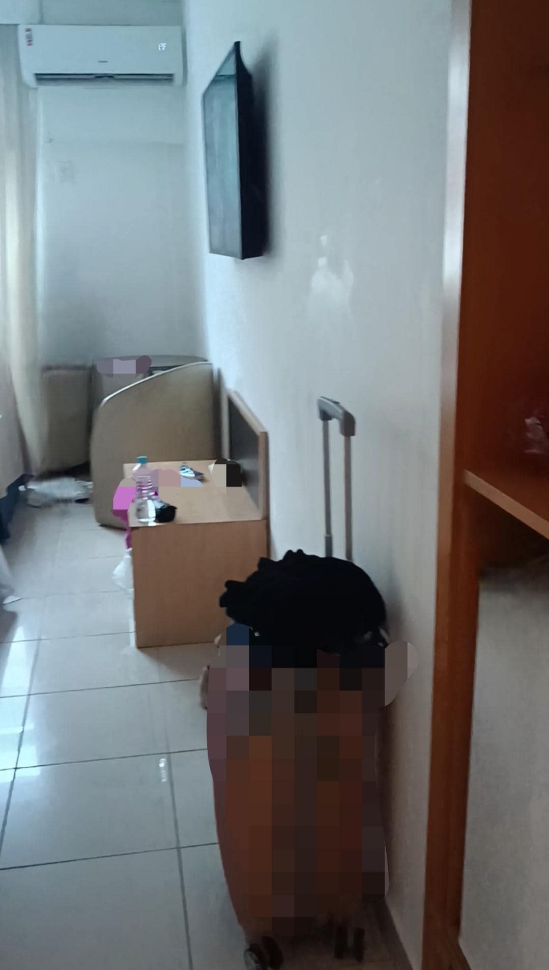 Área do quarto, com televisão, mesa pequena abaixo da televisão, mesa e duas cadeiras no canto e acima um ar-condicionado. 