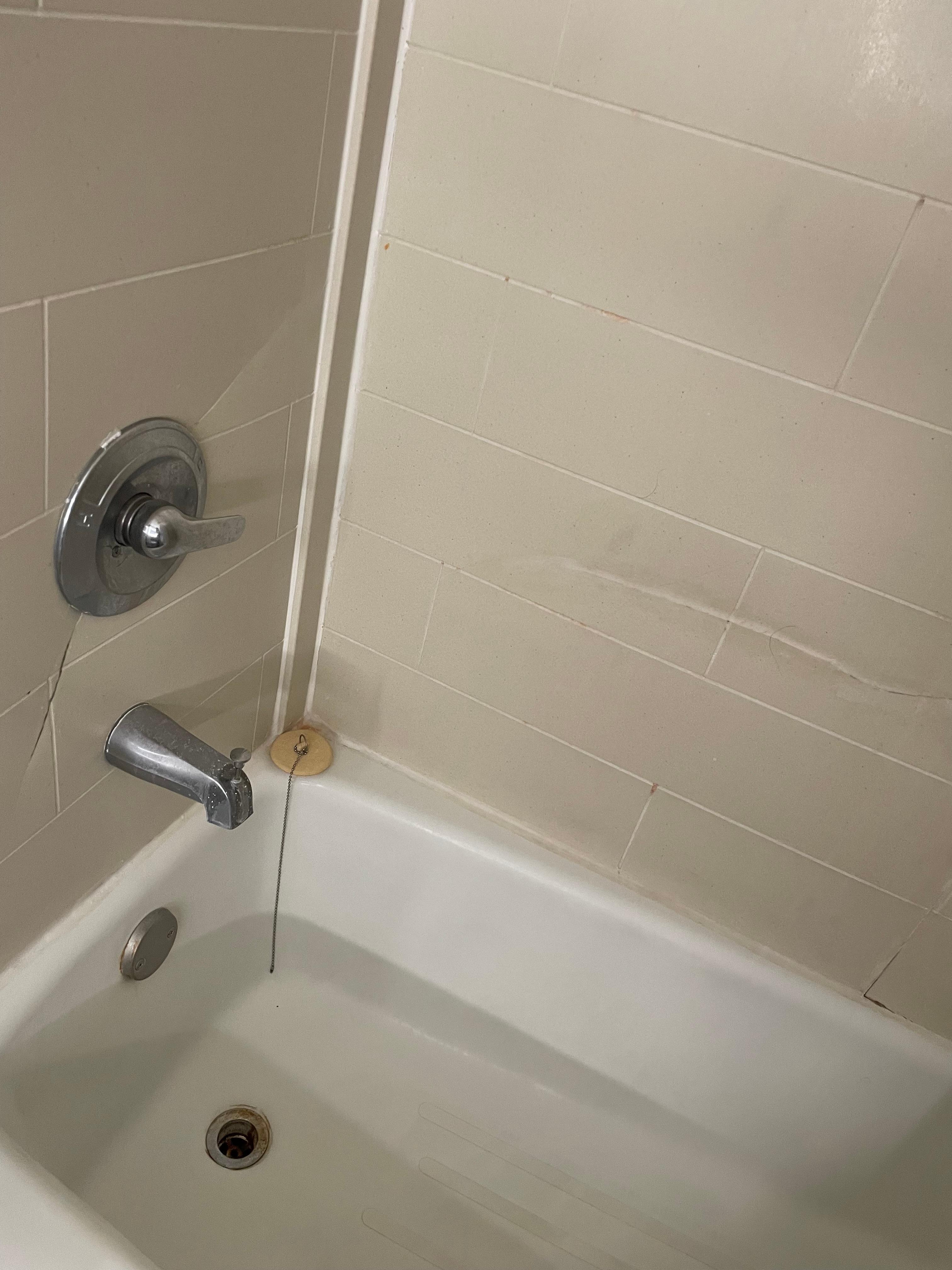 Shower wall with big crack and gash in it.  Plumbing fixtures rusty.