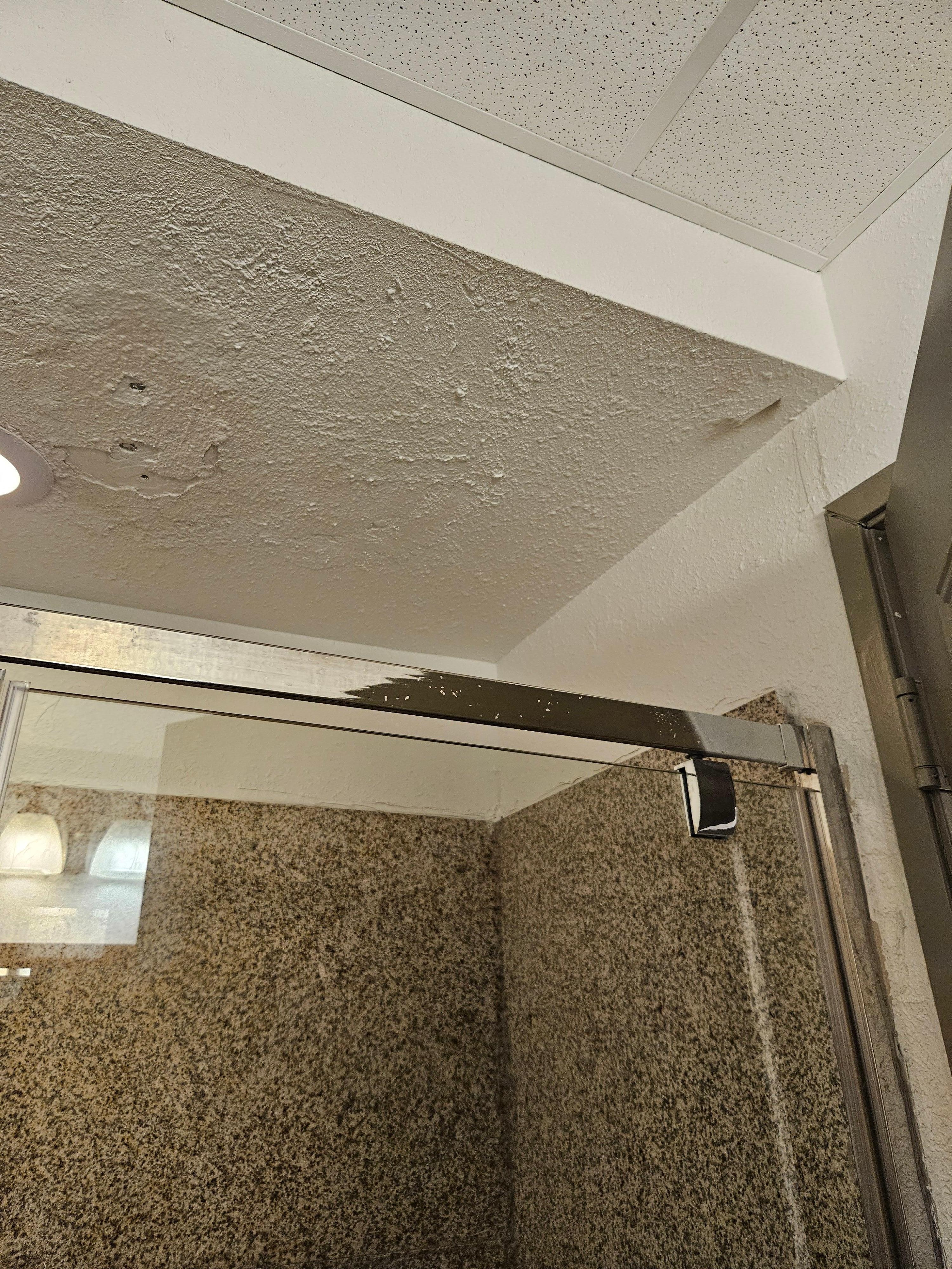 Ceiling in shower needs work and over spray on shower door frame.