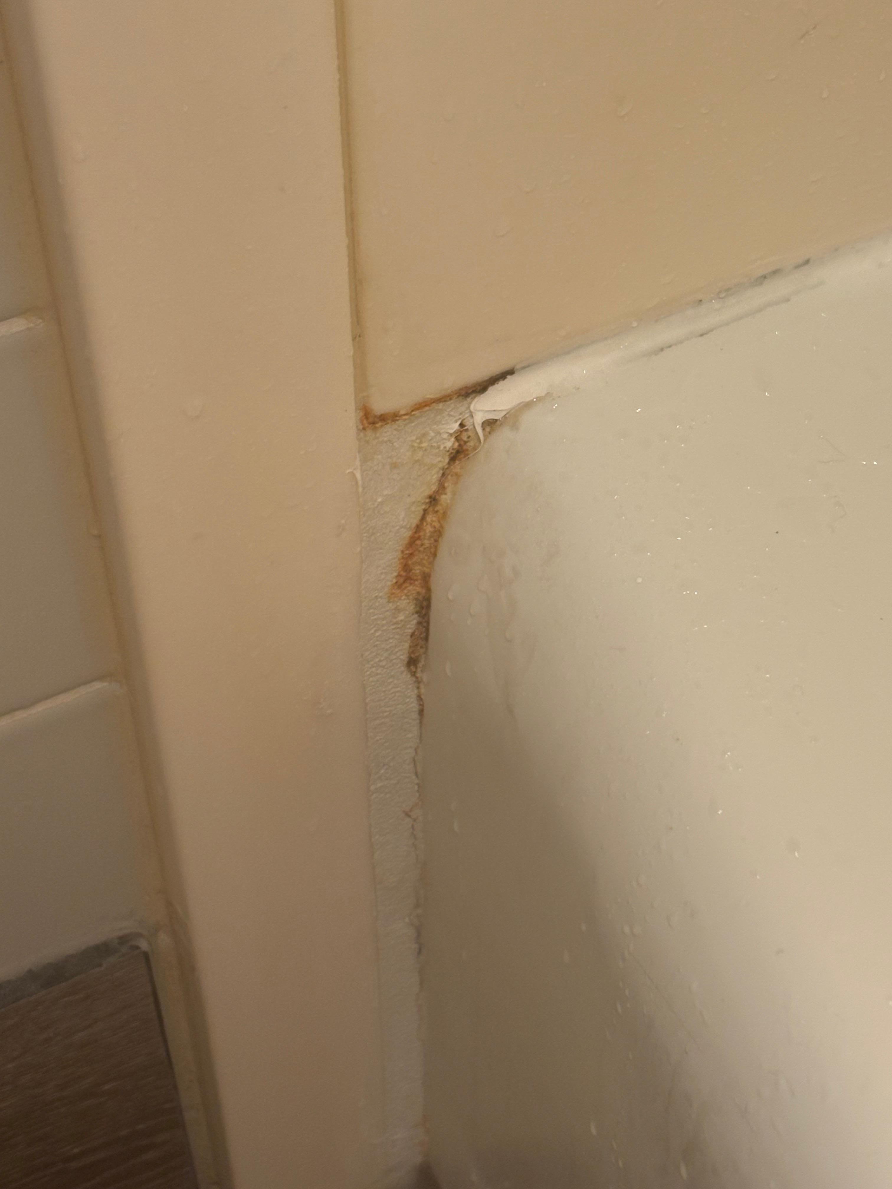 Cracks and rust around the dirty and outdated bathtub/shower.
