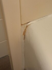 Cracks and rust around the dirty and outdated bathtub/shower.