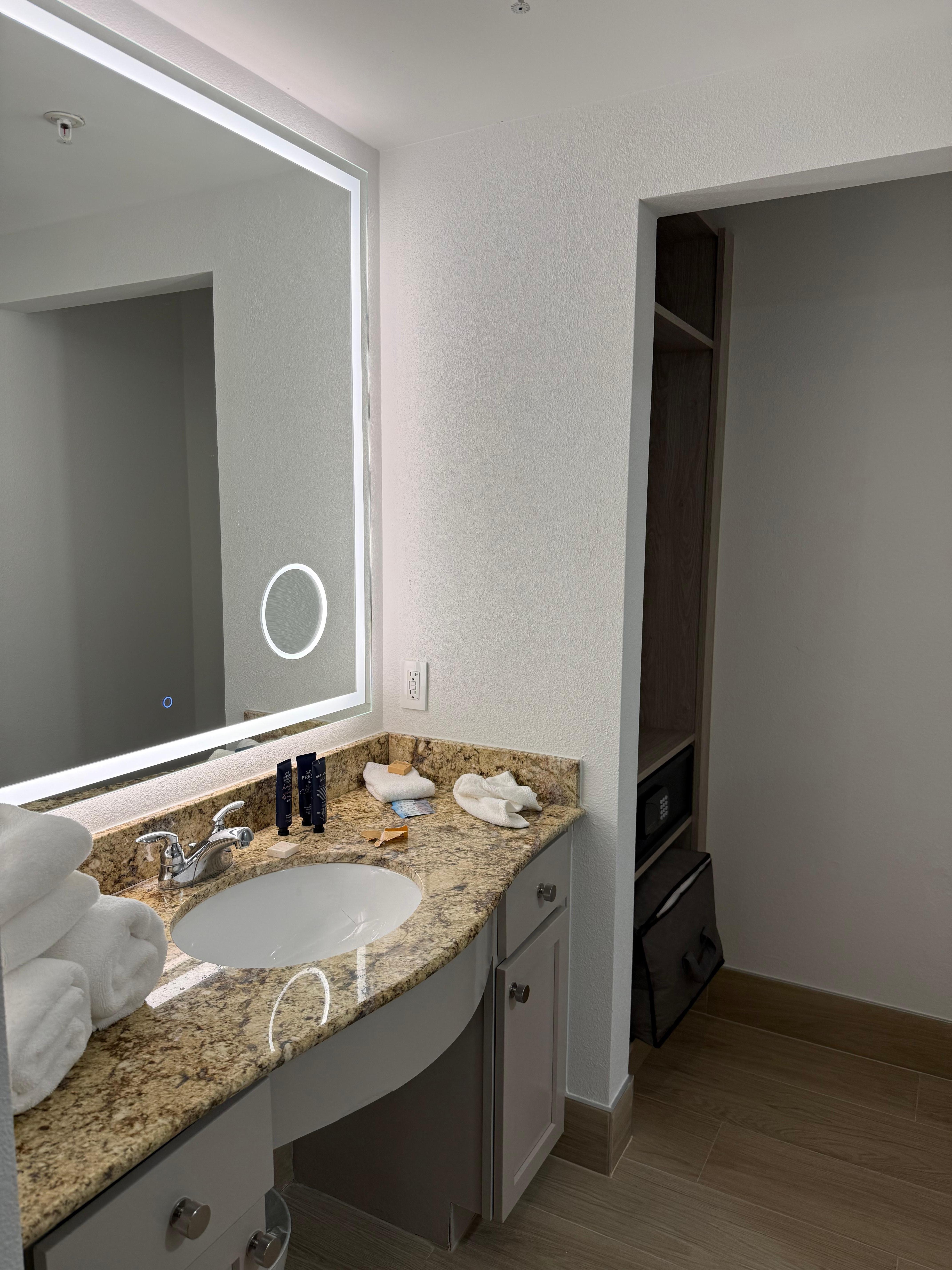 This is the bathroom sink. It has a nice lit mirror. It has an area in the mirror that is actually magnified.