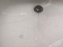 Bathroom sink with crack and a piece of silver tape stuck to the sink.