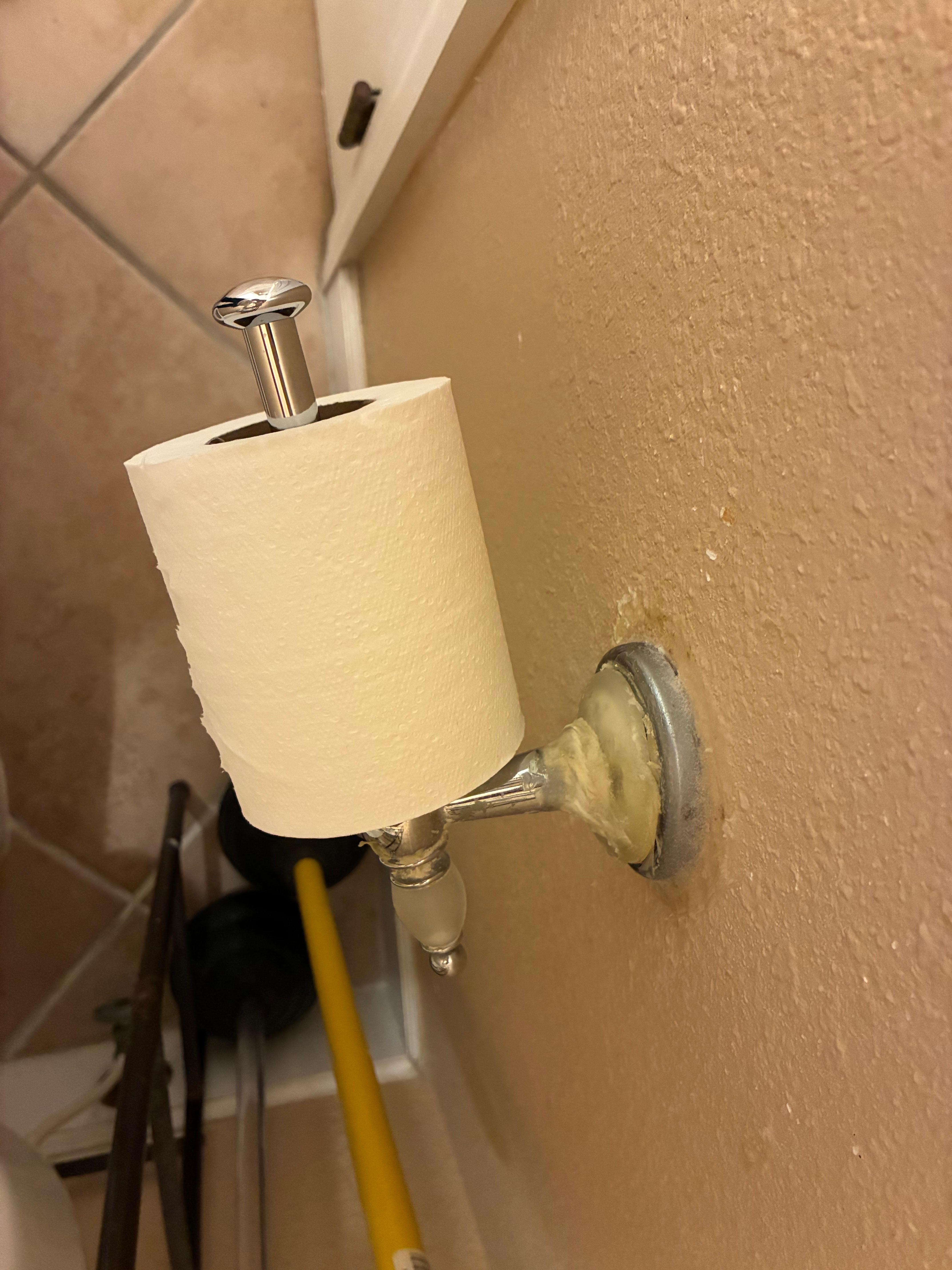 Toilet roll holder affixed to wall with wax or glue
