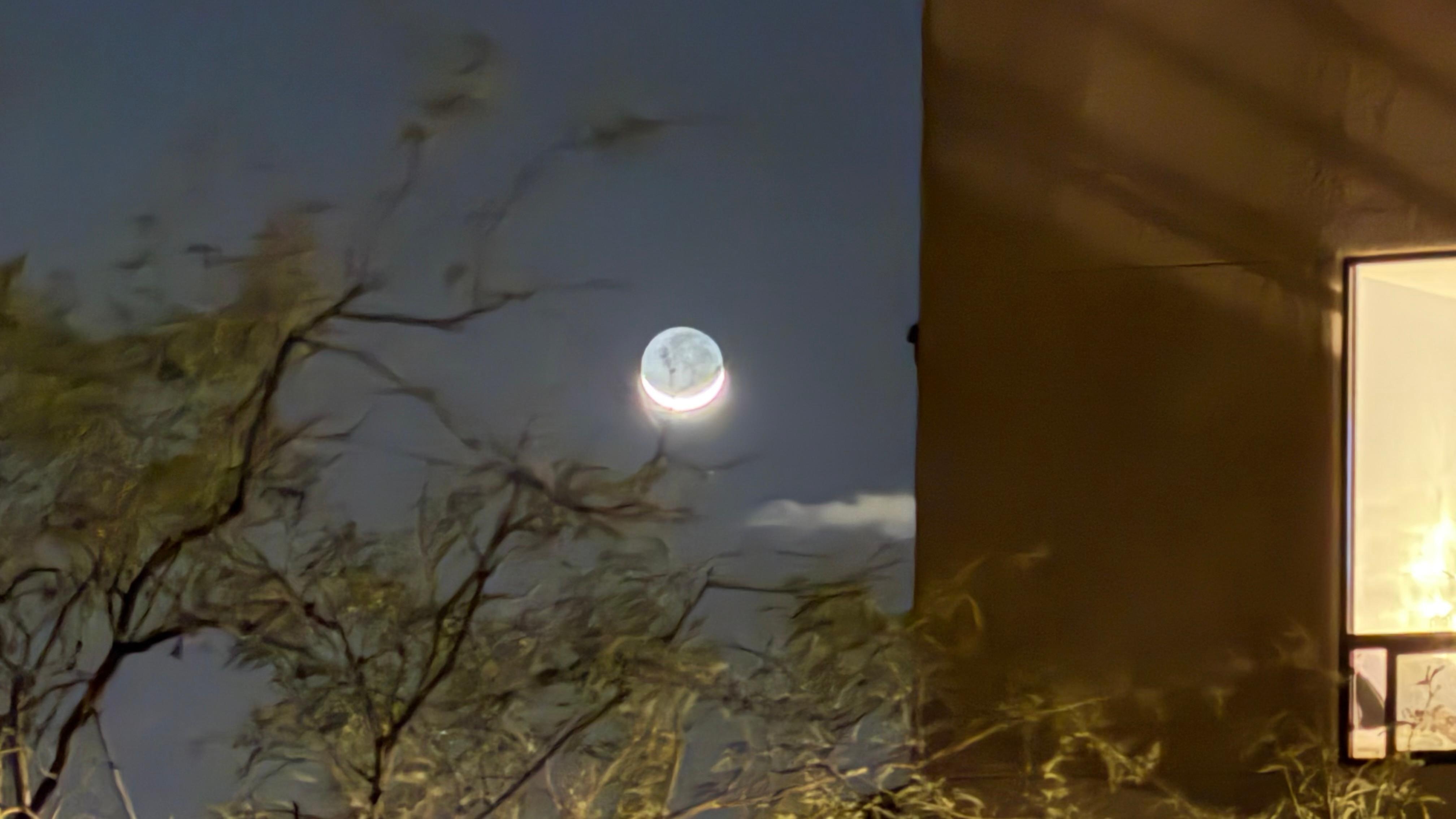 Crescent moon setting next to building