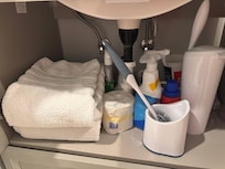 Bath towels under sink next to toilet bowl cleaner & other cleaning supplies is not ok.
