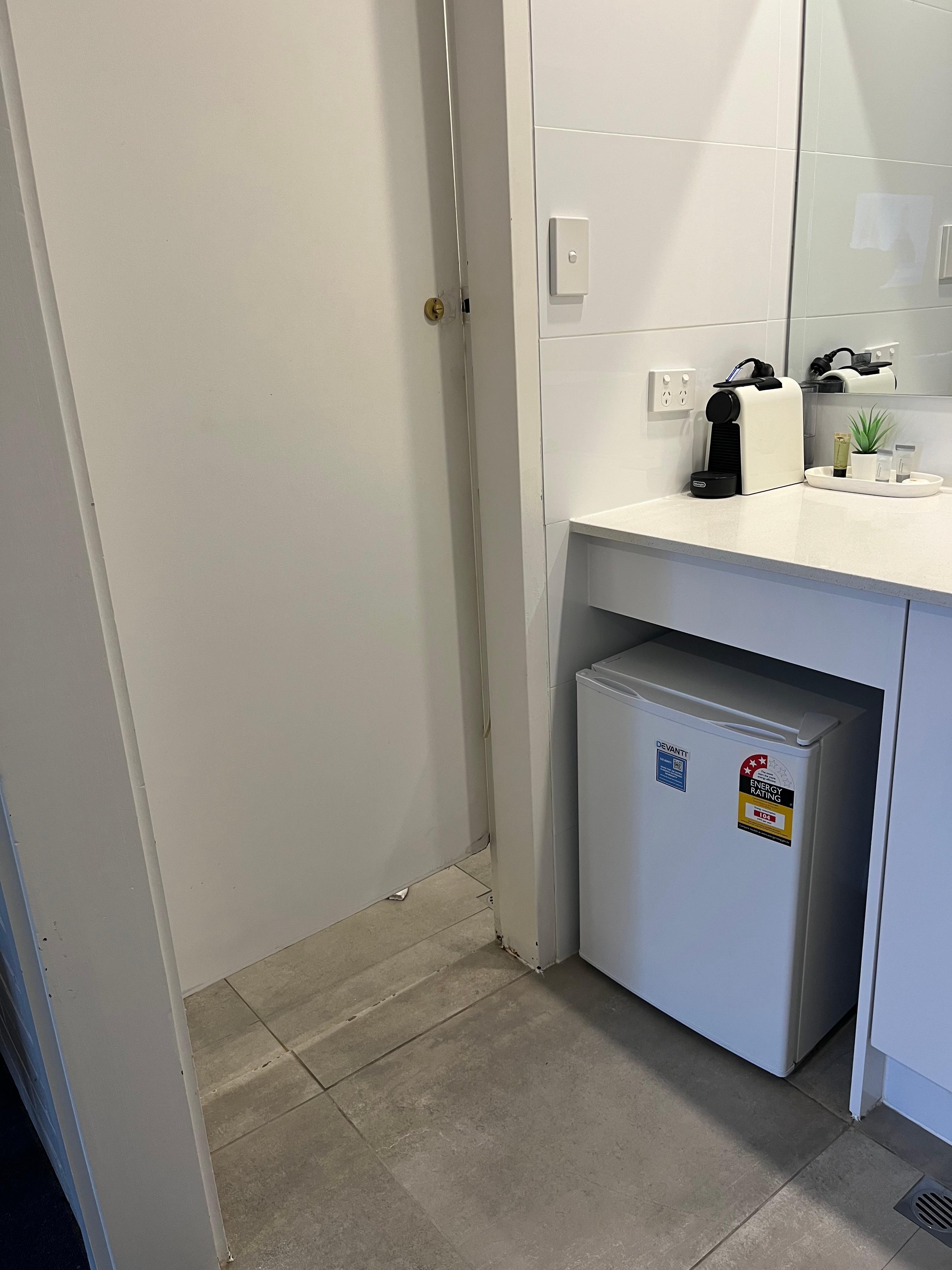Door to shower and fridge in hand basin area