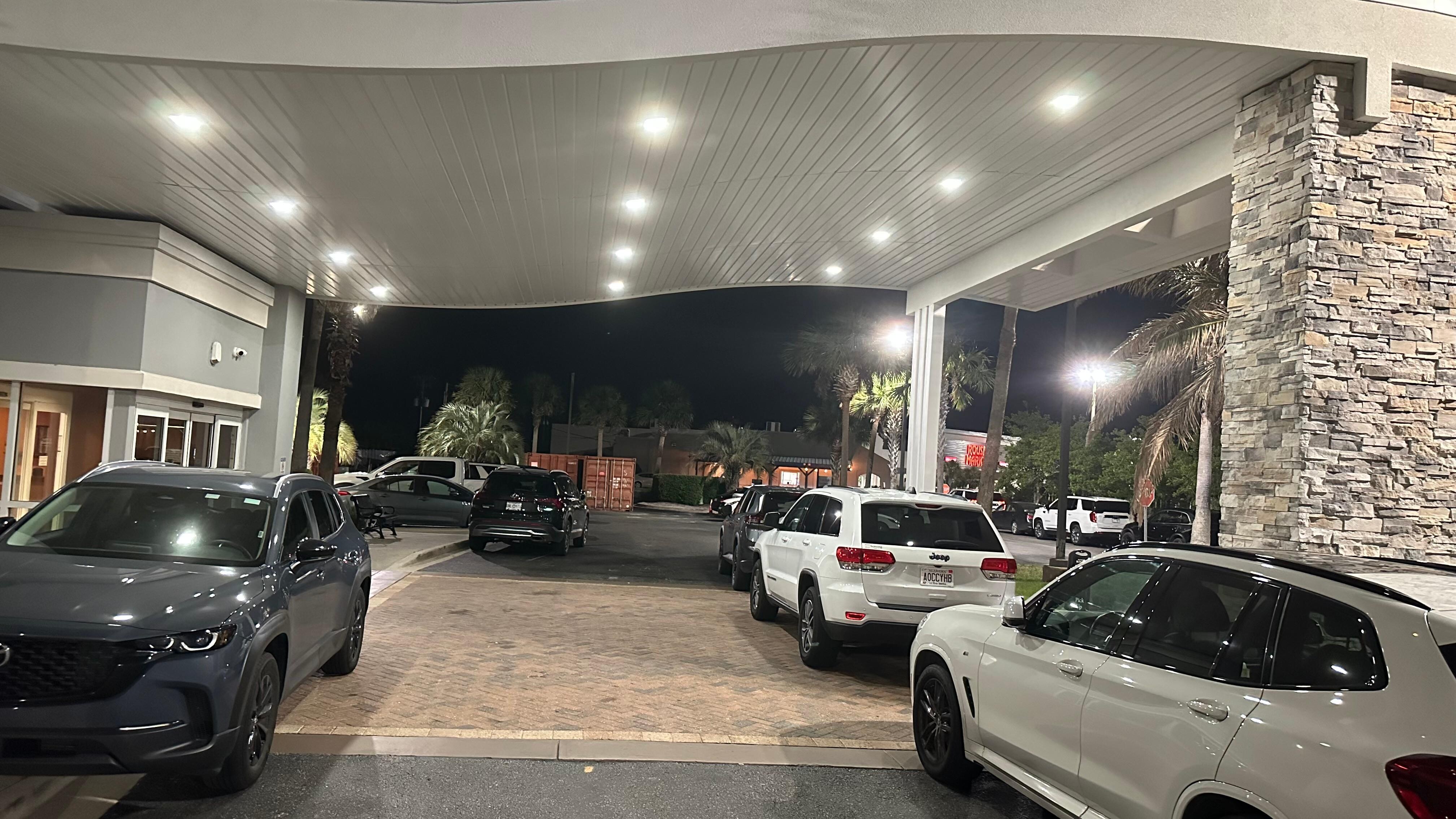 Cars parked in front of hotel drop off due to no parking. Shipping containers and large trash bins take up a lot of parking also