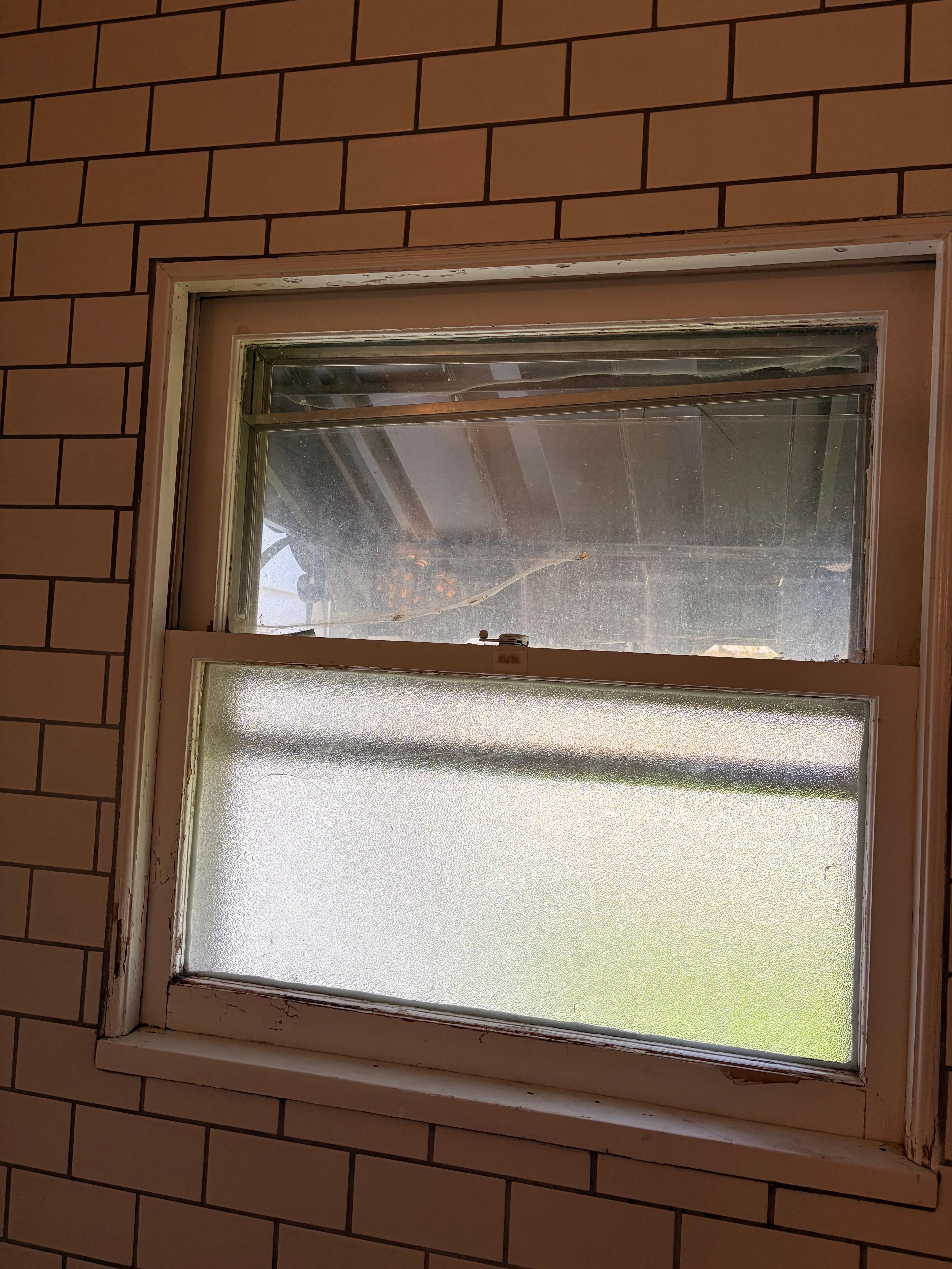 Bathroom window with screen, barely hanging on and in much need of cleaning and repair