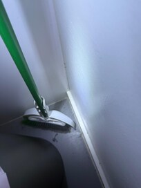 Cobwebs/dead bugs behind broom in the kitchen area.