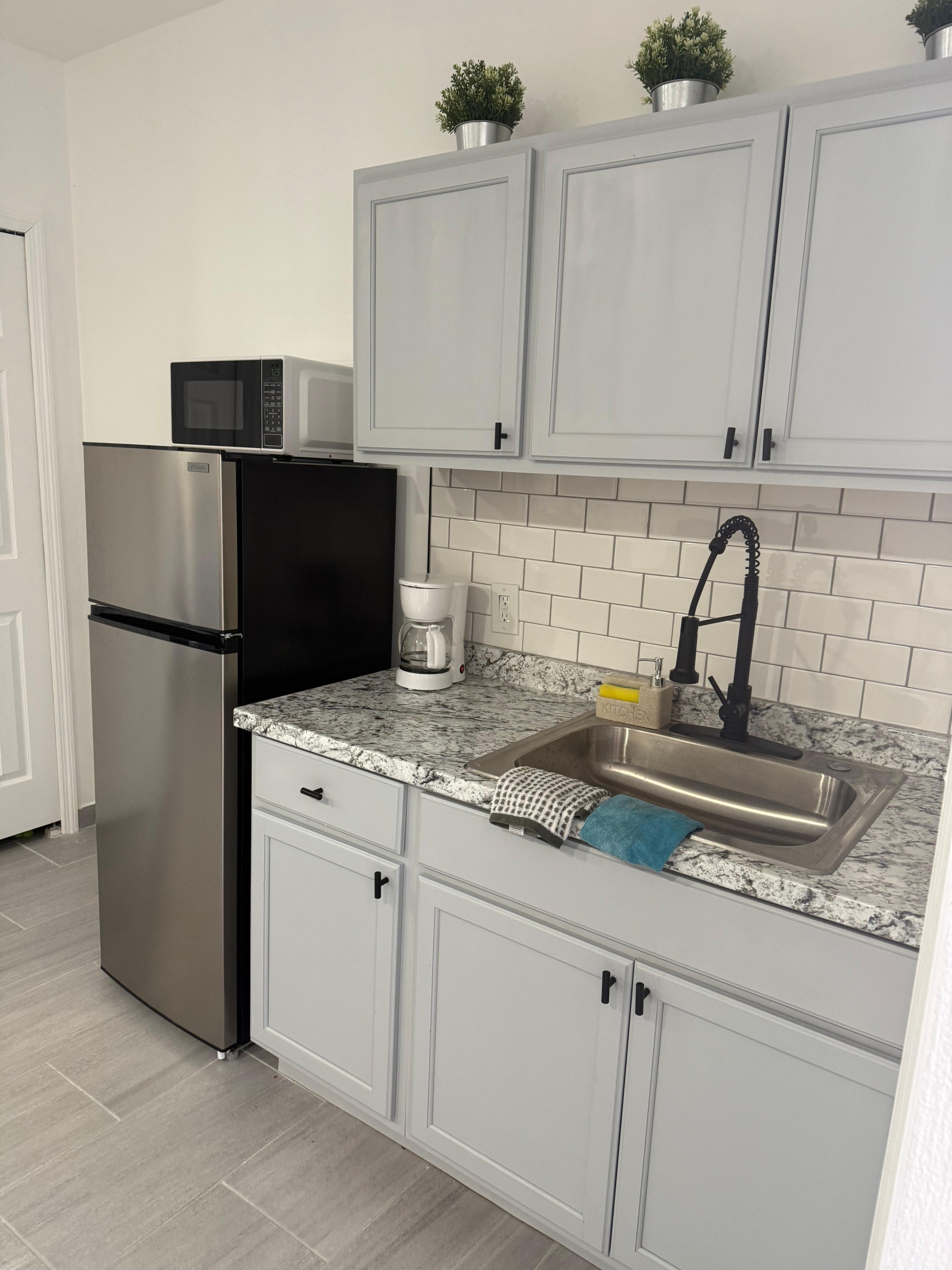 Small but fully equipped kitchen with fridge, microwave, coffee machine and two-burner hot plate and pans stored under the sink. 