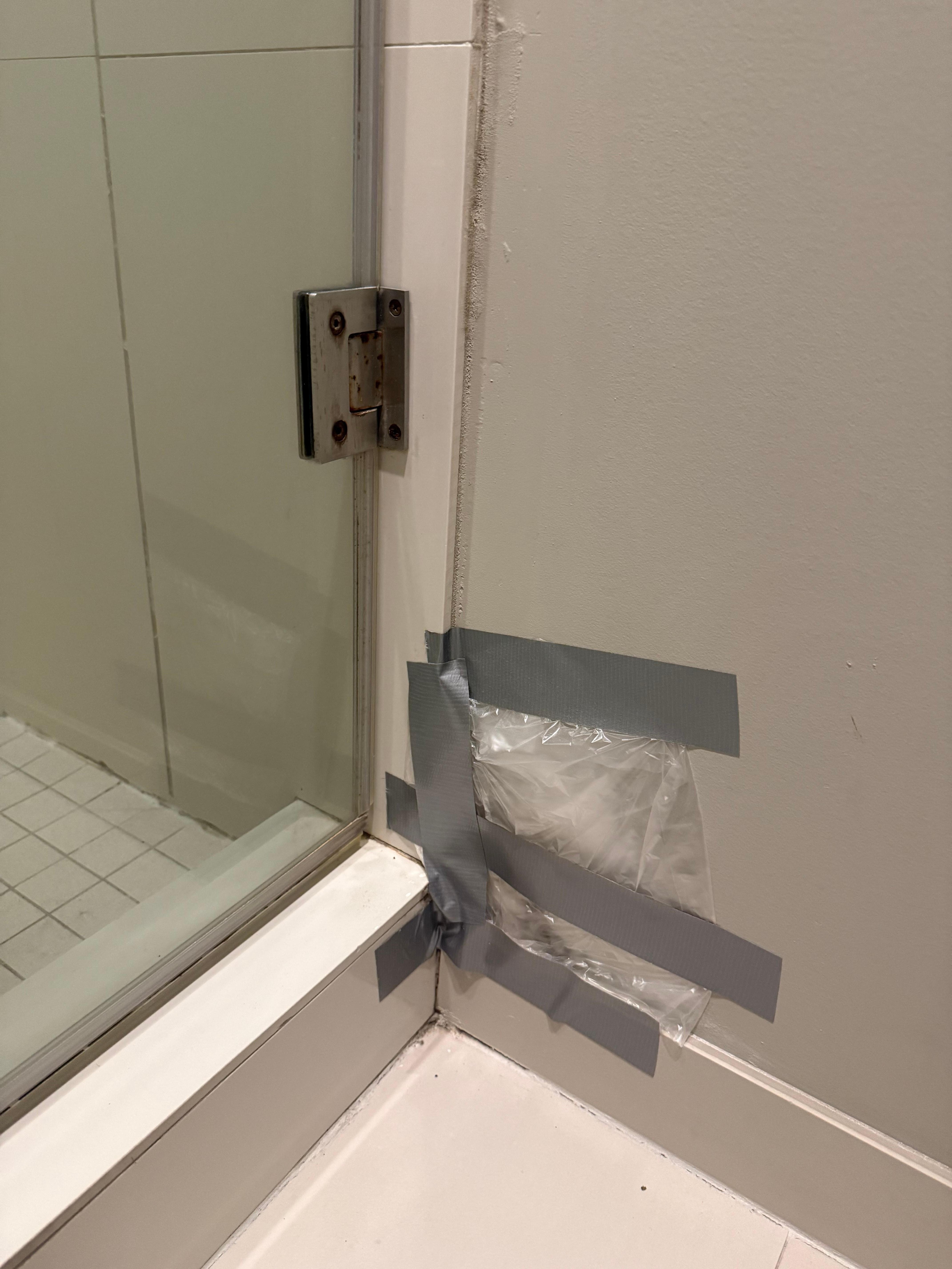 Damaged wall in bathroom sealed with plastic and masking tape