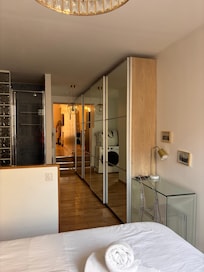 Looking from the bedroom, past the shower, and into the front room of the apartment. Large mirrored closets with ample shelving for folded clothes. Only four hangers, though, for hanging clothes.