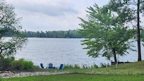 View of firepit and cool Adirondack chairs at end of yard by lake