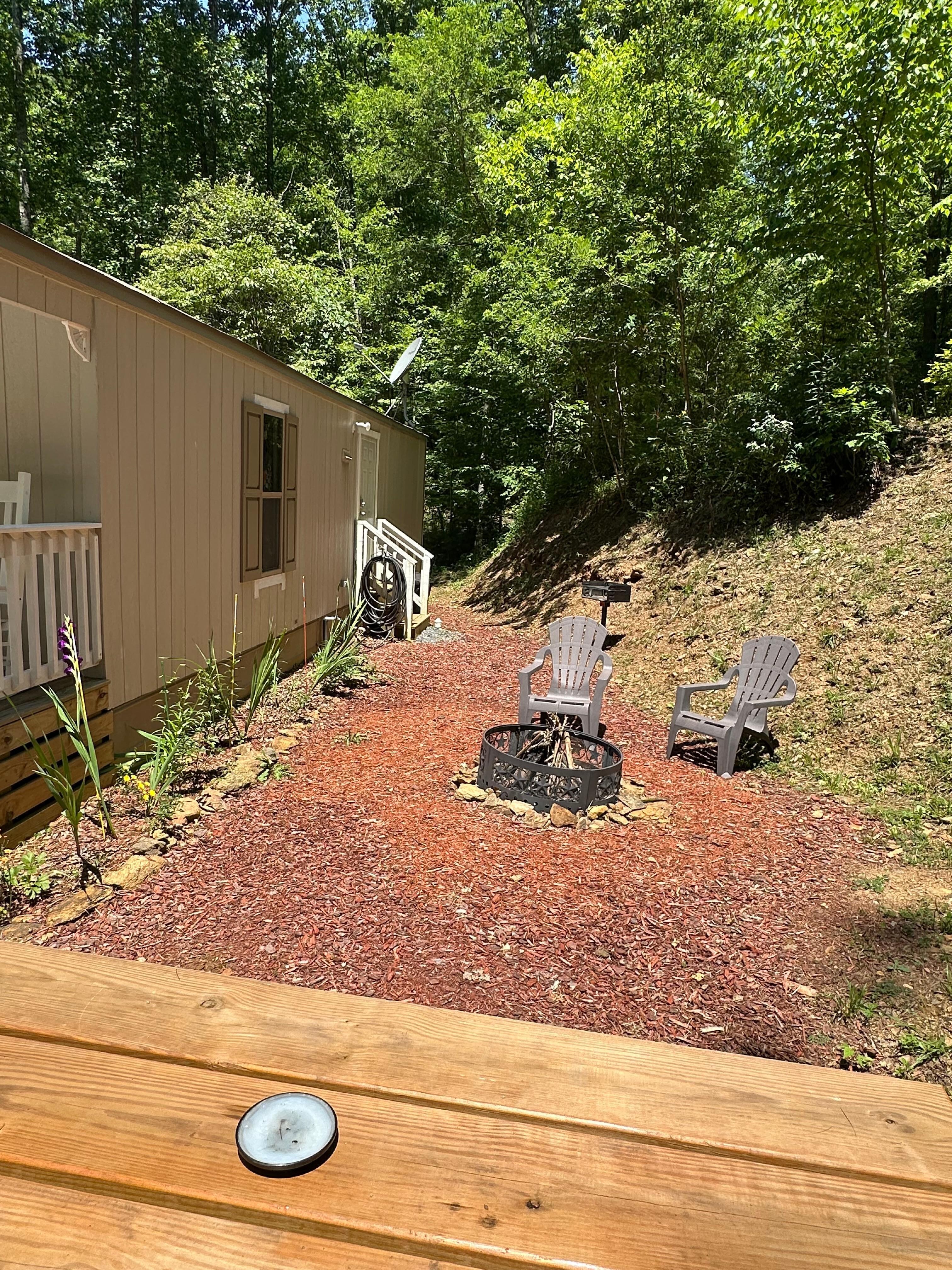 Outdoor area with picnic table, chairs, fire pit with wood and a charcoal grill.