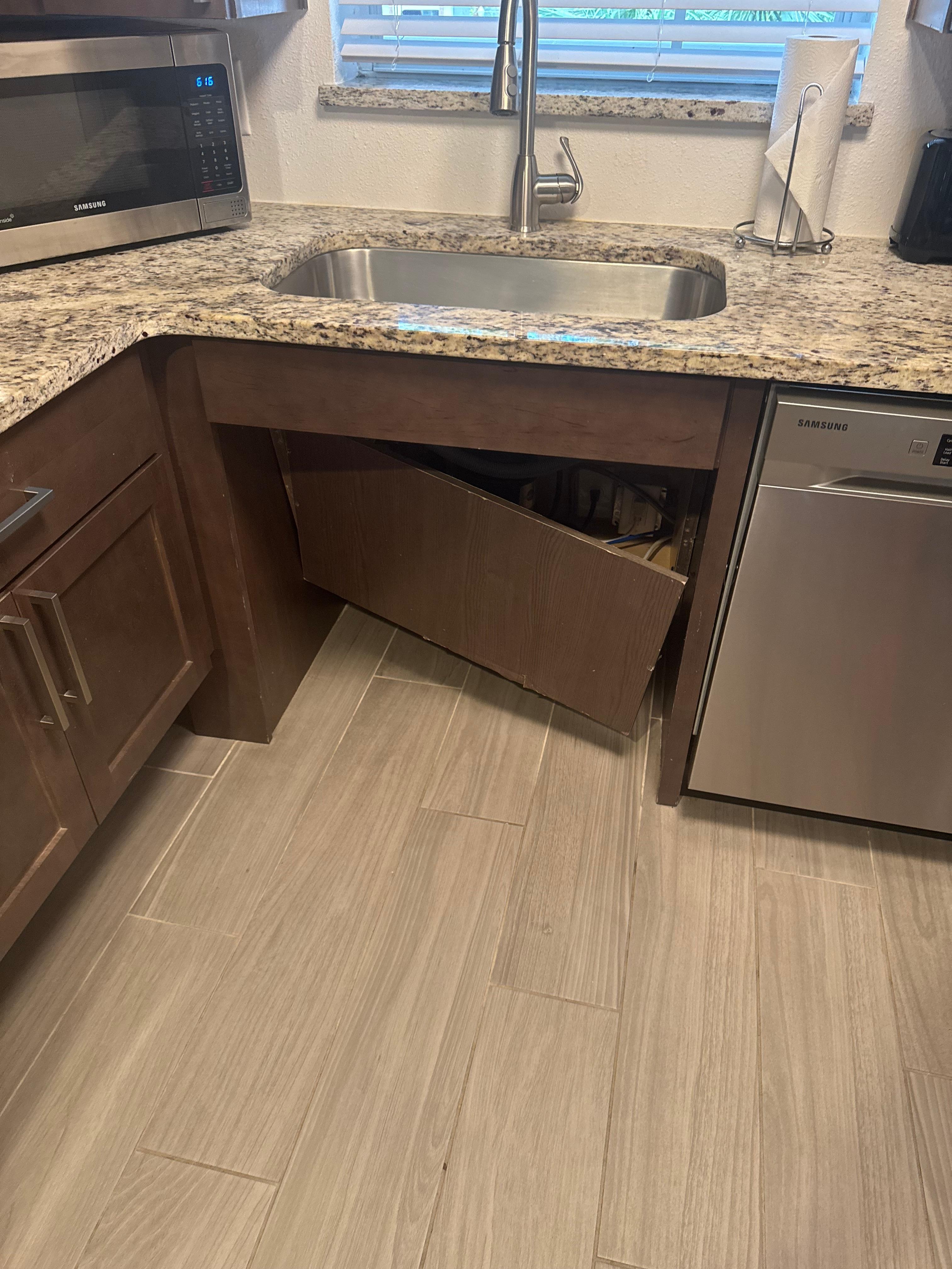 Panel below sink hanging off and exposing plumbing