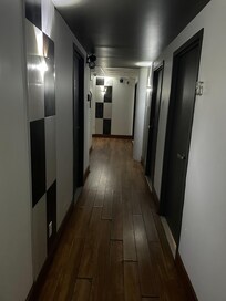 Hallway leading to the pods, washrooms, and common area. Peeling floors and dim lighting. No cameras.