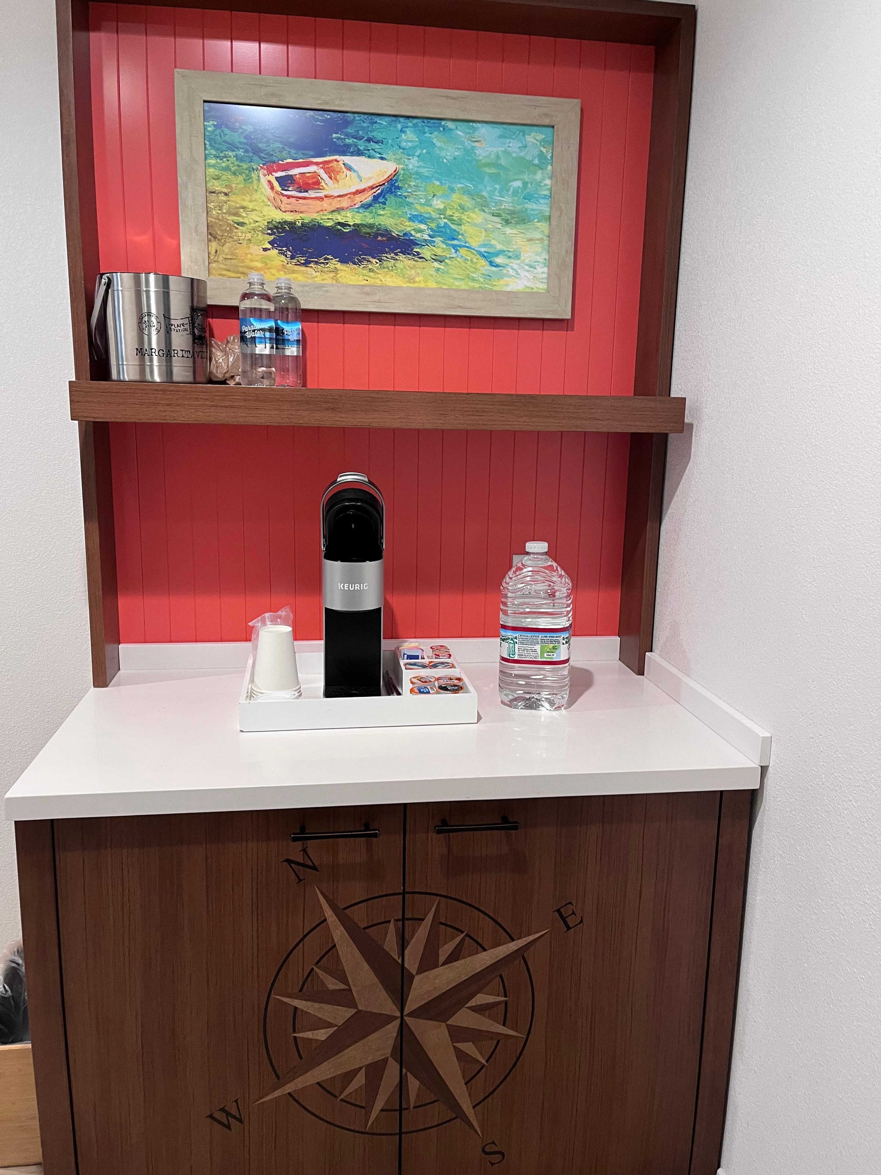 Room fridge below hidden and keurig with coffee, tea, creamer and sugar options 