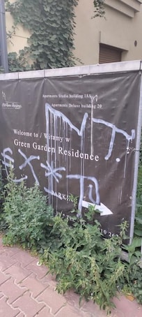 Defaced welcome sign: Graffiti-covered and surrounded by overgrown weeds, clearly showing neglect.