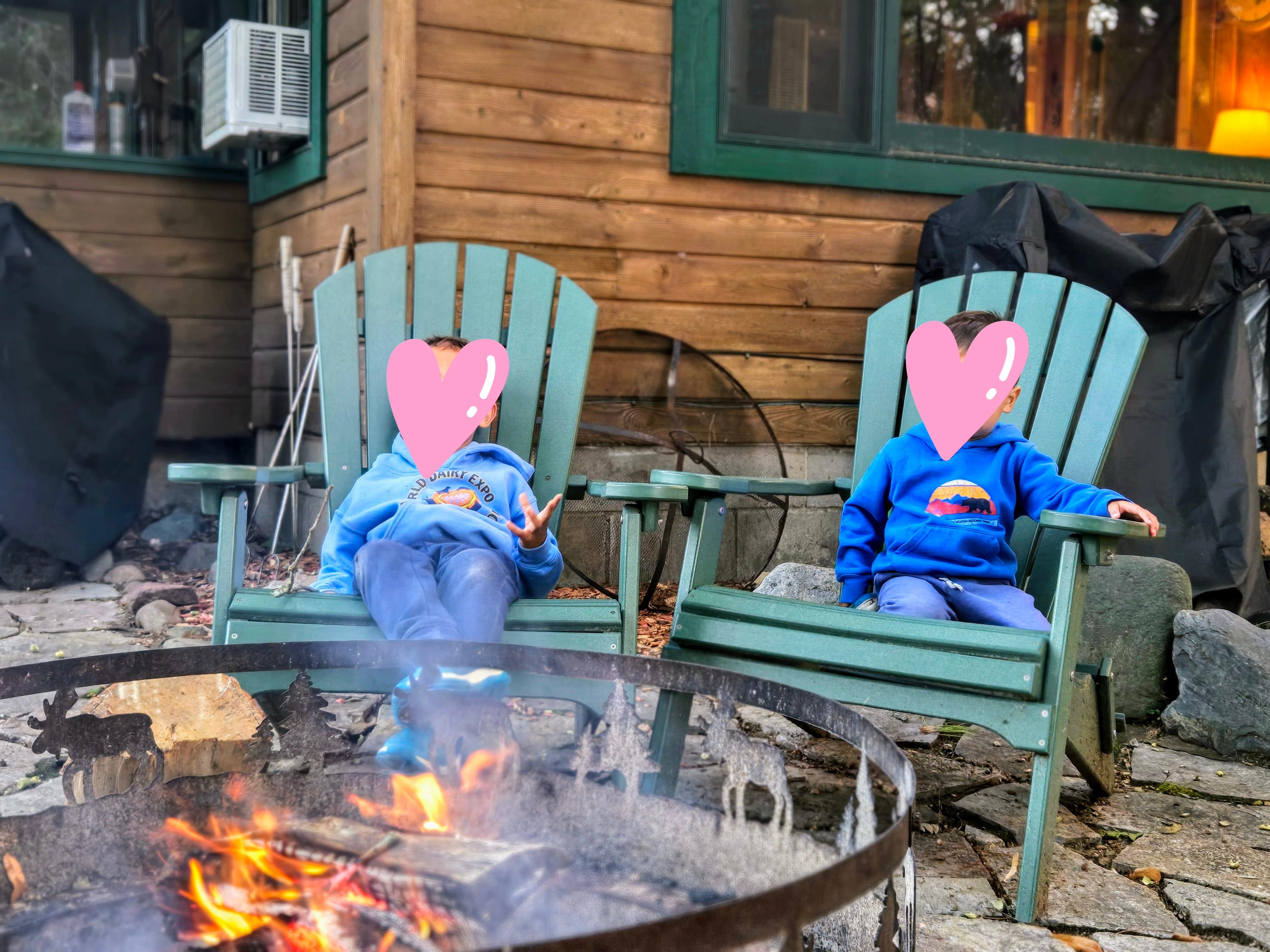 Enjoying the fire, plenty of andirondack style chairs. Tools available for roasting marshmallows. Cabin is in the background.