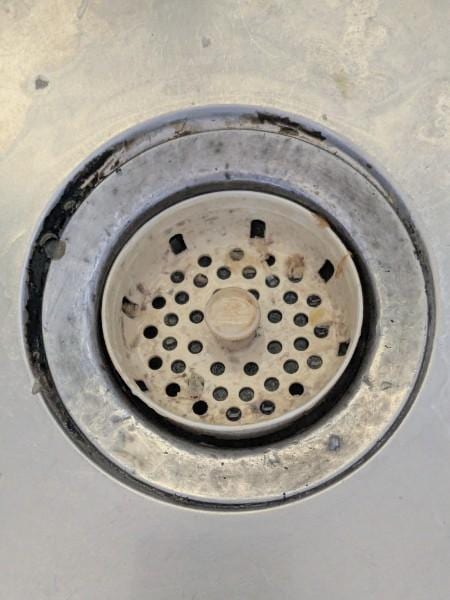 The area around the base of the kitchen sink shows significant rust and accumulated grime. This appears to be long-term build-up that requires deep cleaning and perhaps resealing to prevent further decay.