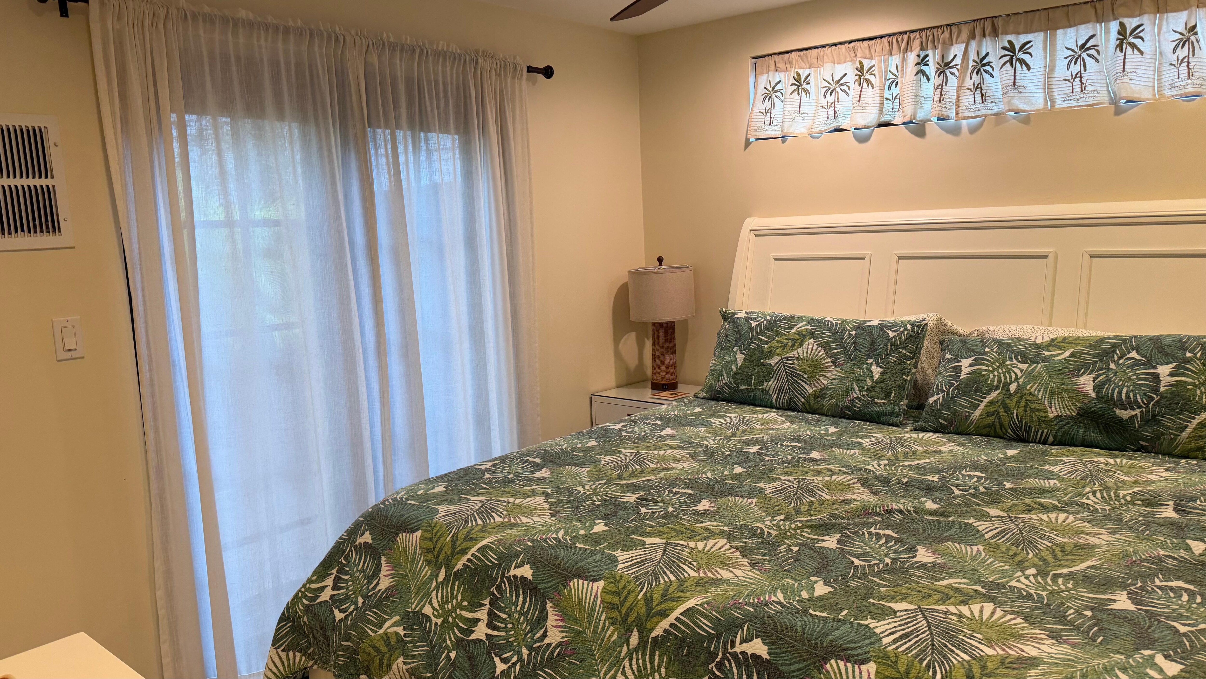 King size bed with ceiling fan, TV and a door opening out to patio. 